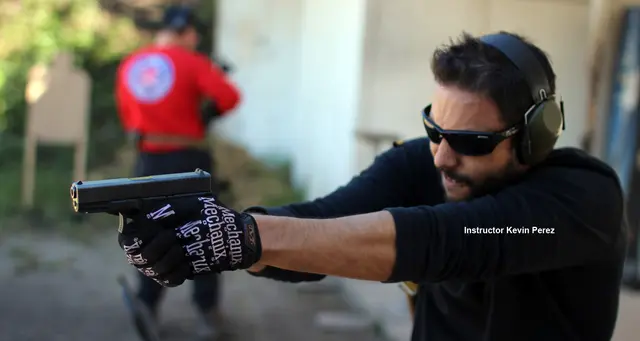 Instructor Kevin Perez shooting a pistol with a two-handed grip while another student shoots downrange